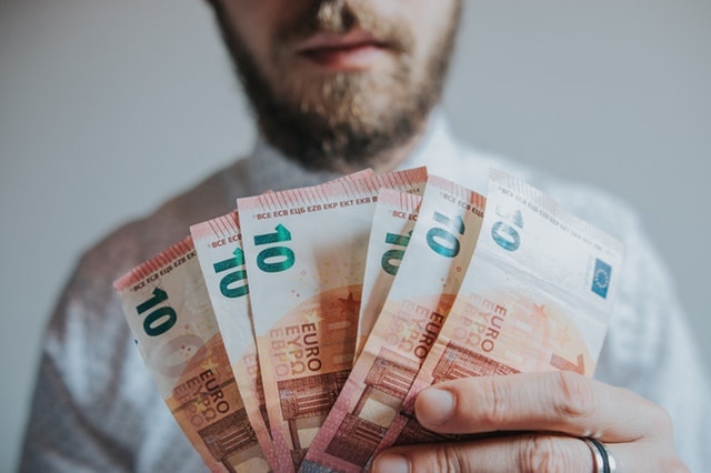 Um homem segura 6 notas de dez euros na mão.